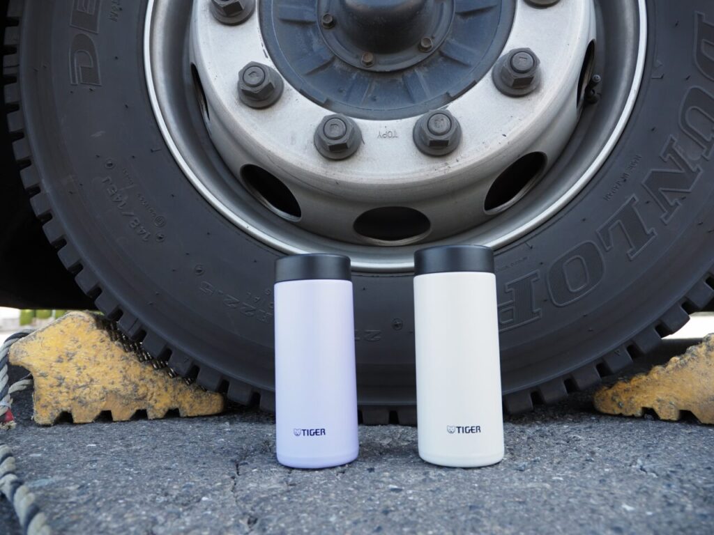 バスのタイヤの前に置かれた、タイガー魔法瓶の画像。